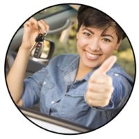 Woman in a car with a key in one hand and giving a thumbs up